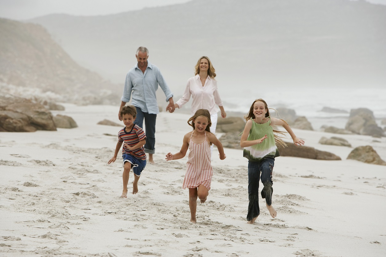 3 healthy kids with parents in background running on beach having fun