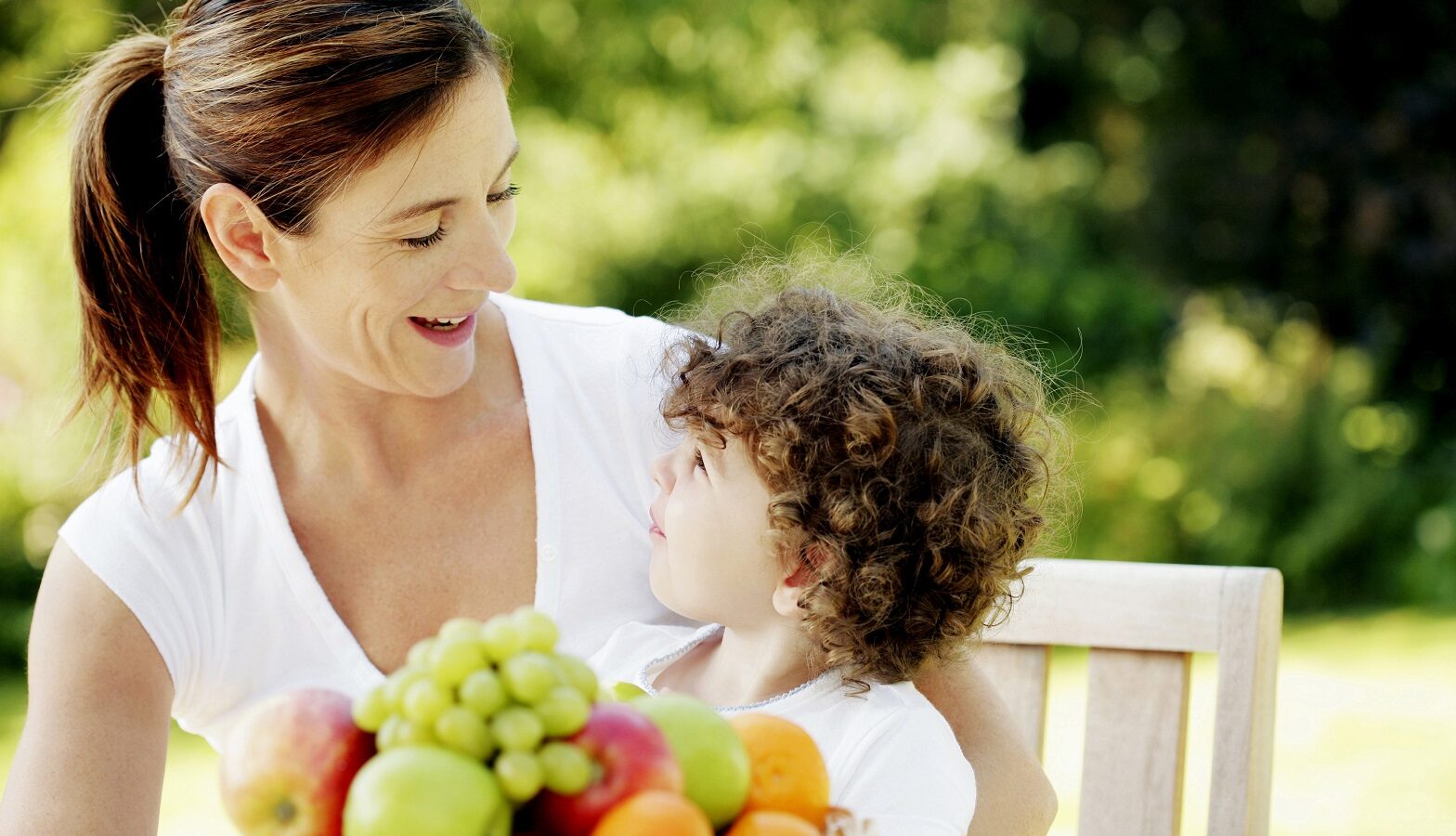 Healthy woman and son sitting outside in front of bowl of fruit